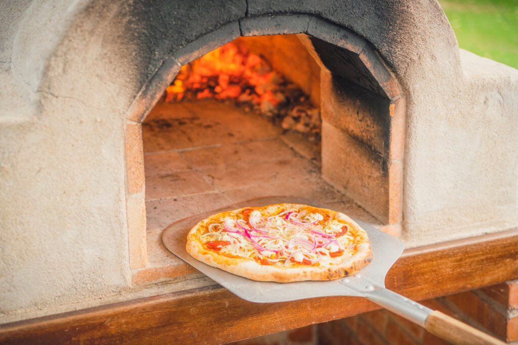 Delicious pizza from a hot outdoor stone oven with fire taken out with a food shovel