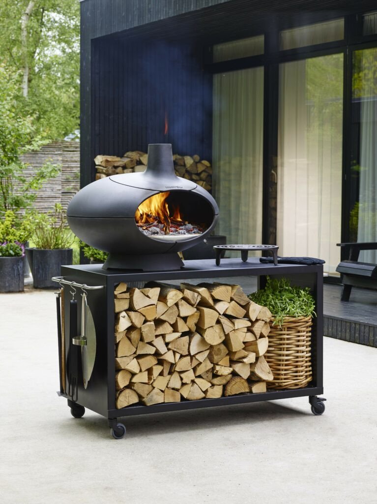 Morso Forno Outdoor Oven with a stand filled with firewood