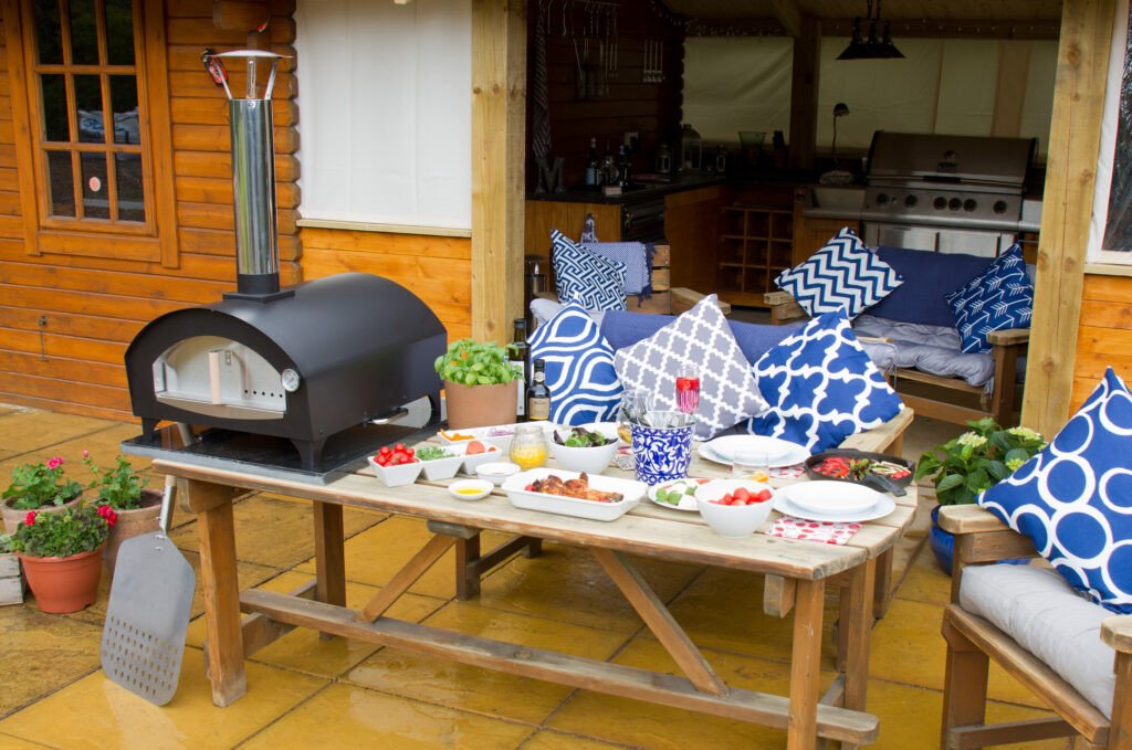 ACR bravo pizza oven with food filled table and outdoor seating with blue cushions
